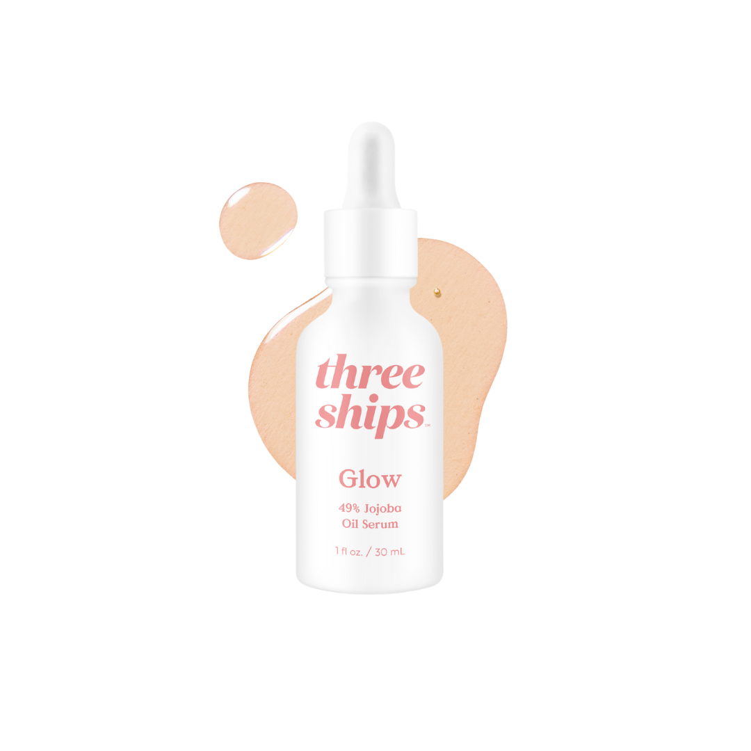 White bottle with pink lettering in front of white background with a splash of oil serum behind it. Three Ships Beauty Glow serum sold at Juniper Skincare in Edina, MN.