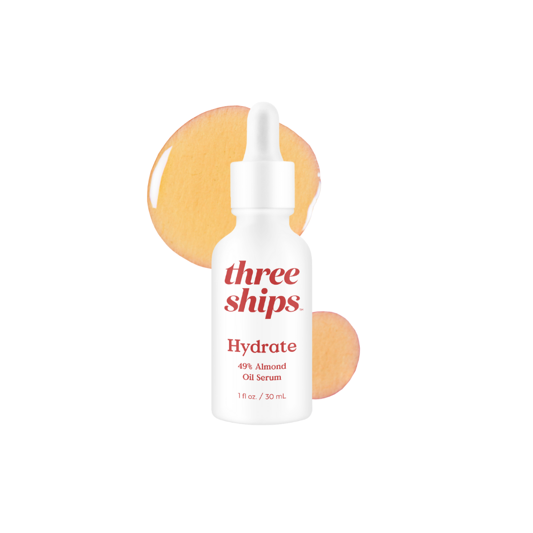 White bottle with red lettering against white background with orange splash of oil behind it. Three Ships Beauty Hydrate Oil Serum sold at Juniper Skincare in Edina, MN.