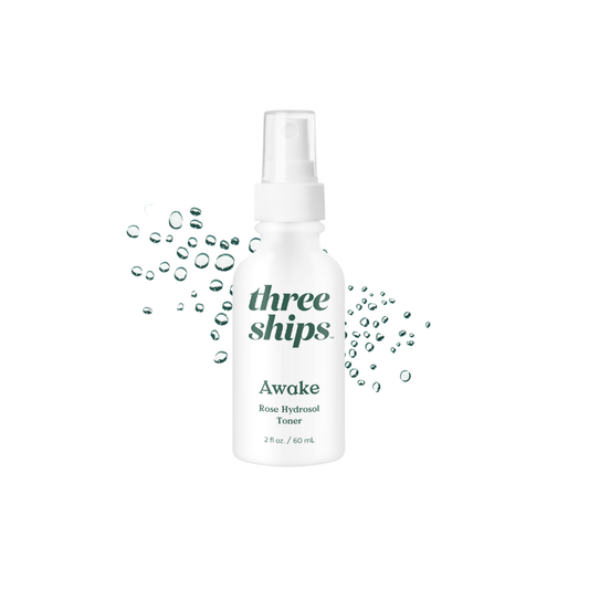 White bottle with green lettering against a white background with liquid droplets behind it. Three Ships Beauty Awake Hydrosol Toner sold at Juniper Skincare in Edina, MN.