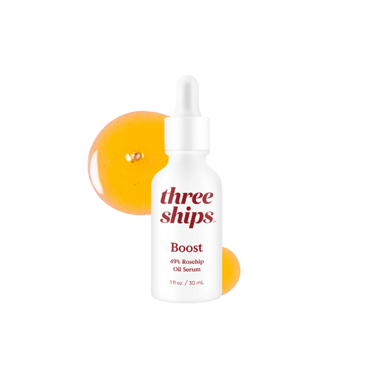 White bottle with red lettering against white background with orange oil splash behind it. Three Ships Beauty Boost Oil Serum sold at Juniper Skincare in Edina, MN.